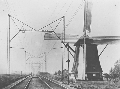886032 Gezicht op een molen langs een geëlektrificeerde spoorlijn met vlinderportalen.